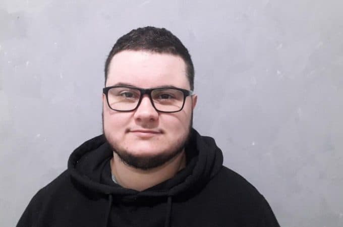 No centro da imagem, em plano médio, há um homem branco. Ele usa óculos pretos e um moletom, também preto. Trata-se de Kadu, um dos personagens da reportagem.