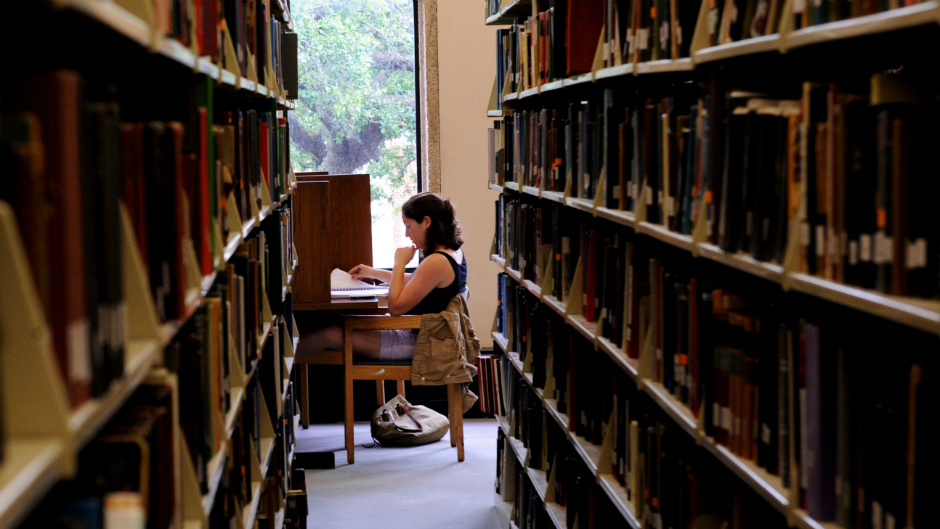 Mulher lendo sozinha ao fundo de uma biblioteca