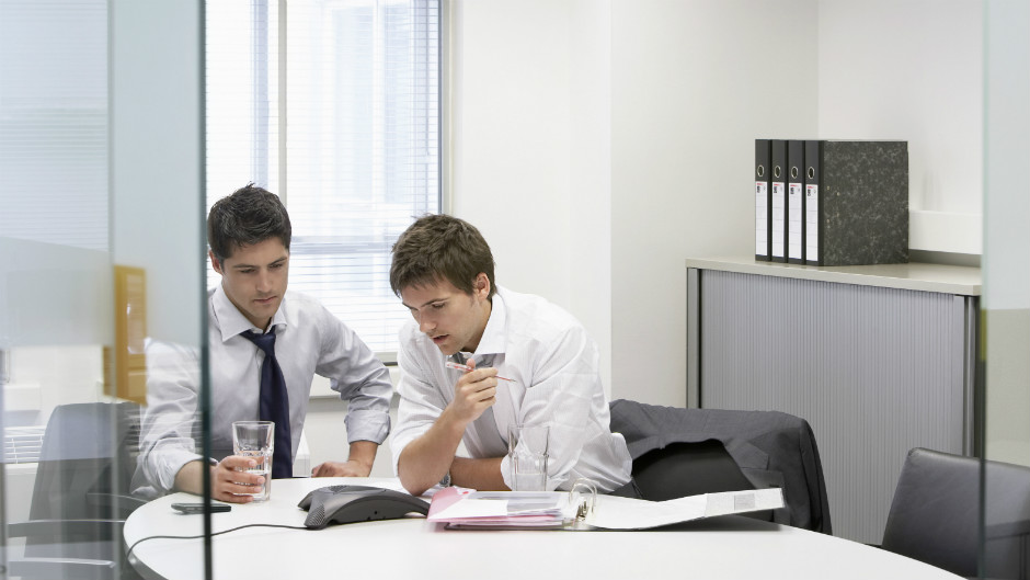 Homens participam de conference call em sala de reunião