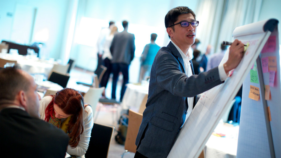 homem asiático tomando notas de reunião em flipchart [matéria sobre carreira em consultoria]