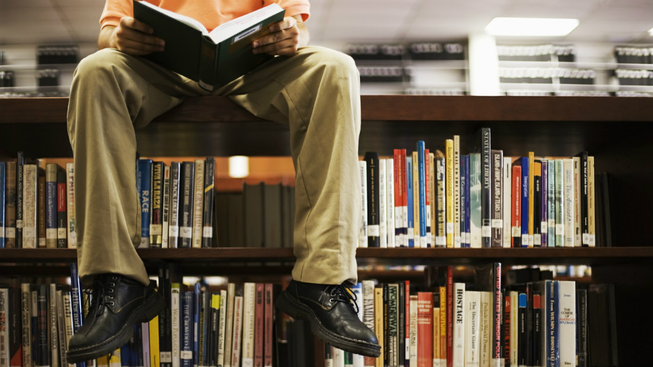 homem lendo sentado sobre estante em biblioteca