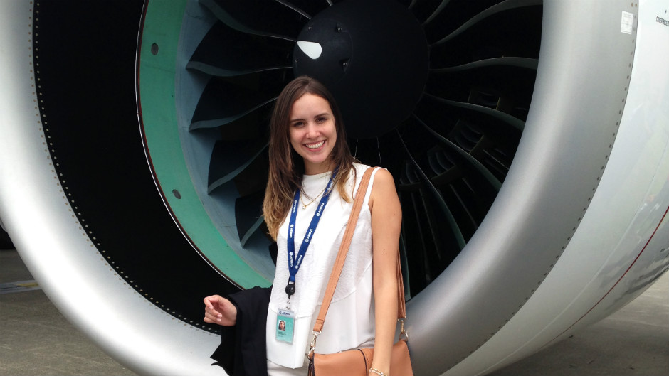 Jovem moça faz pose em frente a turbina de avião