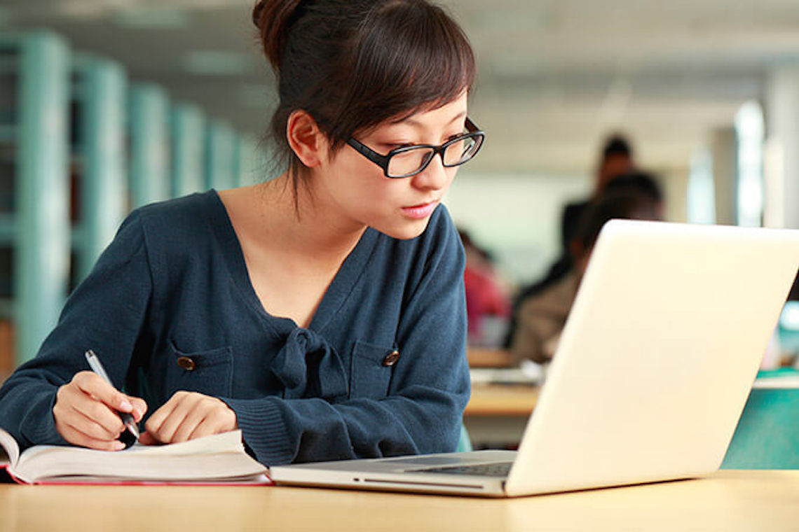 Jovem mulher estudando em uma biblioteca com um caderno e um laptop