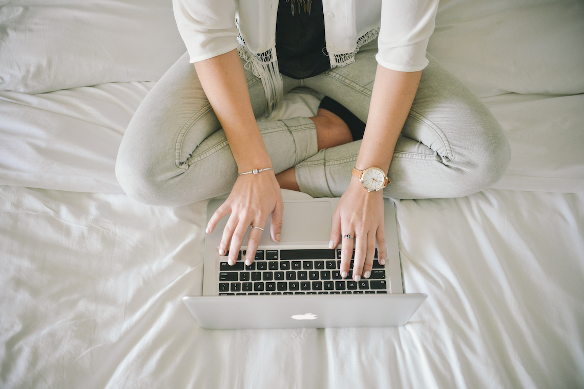 Mulher trabalhando com um laptop de pernas cruzadas na cama