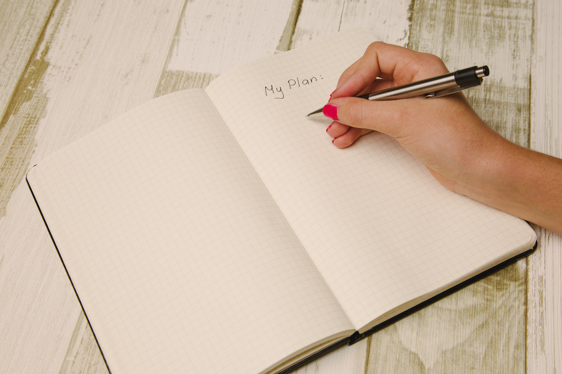Mão feminina segurando caneta e escrevendo um plano num papel