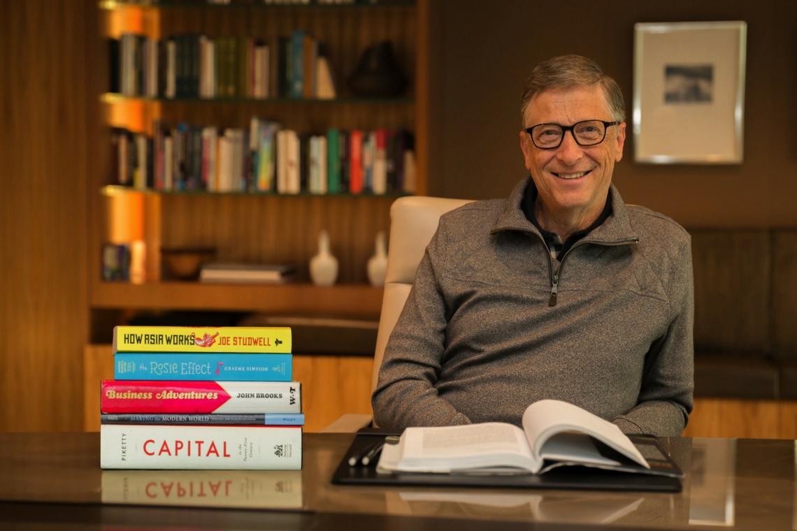 Bill Gates ao lado de uma pilha de livros.