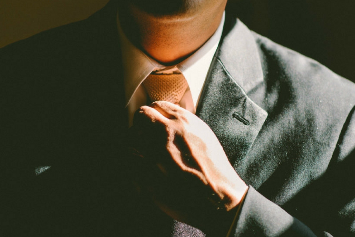 Mão ajeitando a gravata em um terno.