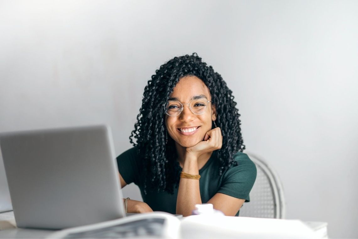 jovem negra sorrindo sentada em frente a um notebook