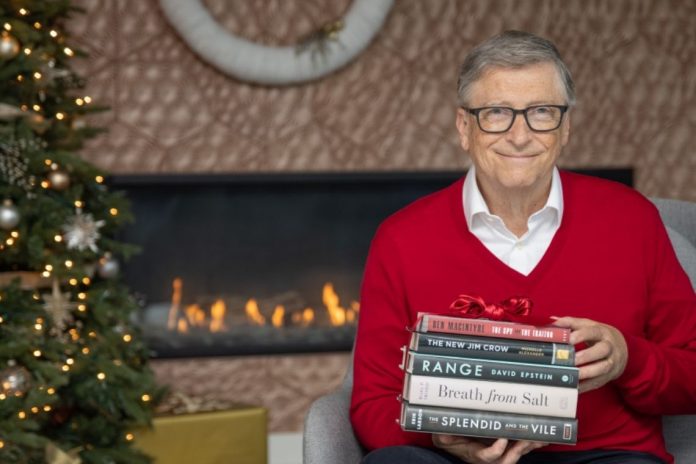 Bill Gates segurando pilha de livros que recomenda em 2020
