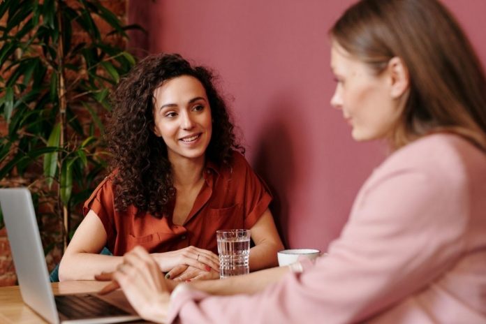 Duas mulheres conversam, frente a frente, em uma entrevista de emprego.