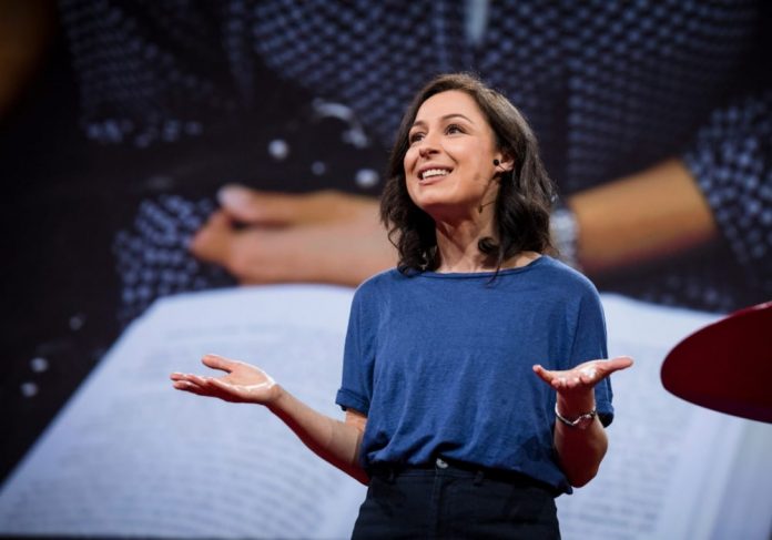 Jornalista Manoush Morodi, uma mulher branca, usa uma camisa azul e fala a uma plateria do Ted Talks sobre a relação entre o tédio e as boas ideias