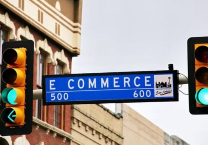 Uma placa azul grafada com a expressão e-commerce aparece ao lado de um semáforo com a luz verde acesa. Mercado de e-commerce