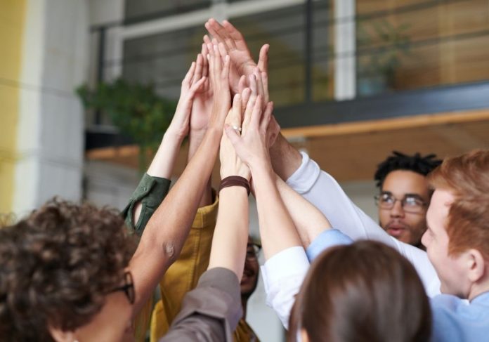 Pessoas tocam as mãos umas das outras no alto da imagem. Elas representam a cultura organizacional de uma empresa.