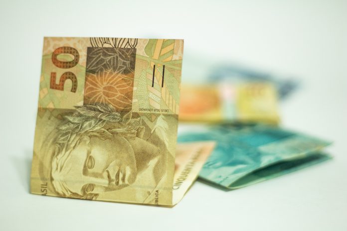 Imagem mostra um punhado de notas de 50 e 100 reais dobradas. Elas são representação do seguro-desemprego.