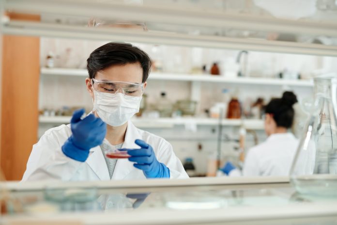 Em um laboratório, uma pessoa com roupa de cientista manuseia um conta-gotas